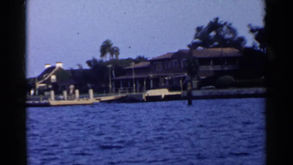 California marina view from the water with waterfront houses, palm trees, dock posts, and a small boat near shore.