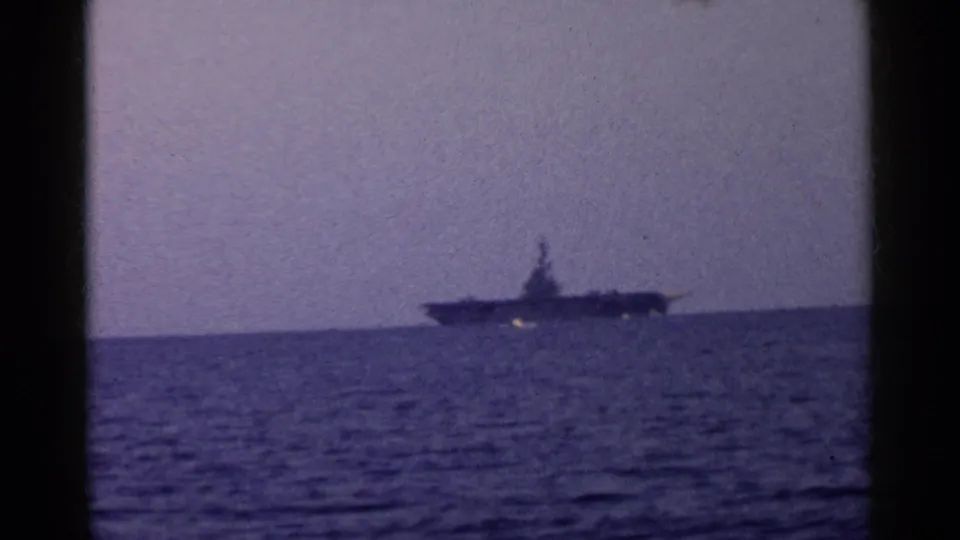 A soft 8mm view of a large naval vessel offshore in California, with rippled ocean in the foreground and faded blue-purple color.