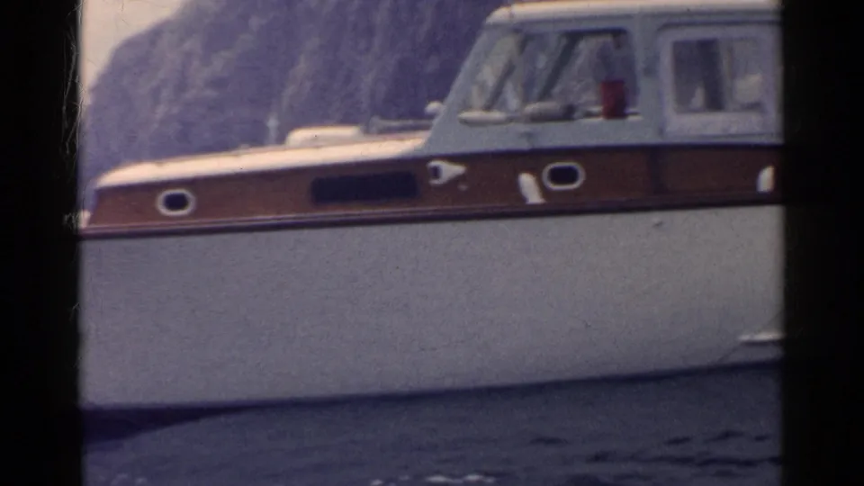 1955 California home-movie frame focusing on the cabin cruiser’s hull and cabin as the rowboat activity moves out of view.