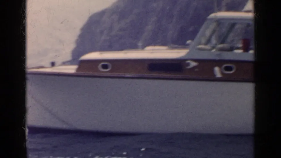 1955 California boating frame showing the cabin cruiser from the side with calm water and a rocky shoreline in the background.