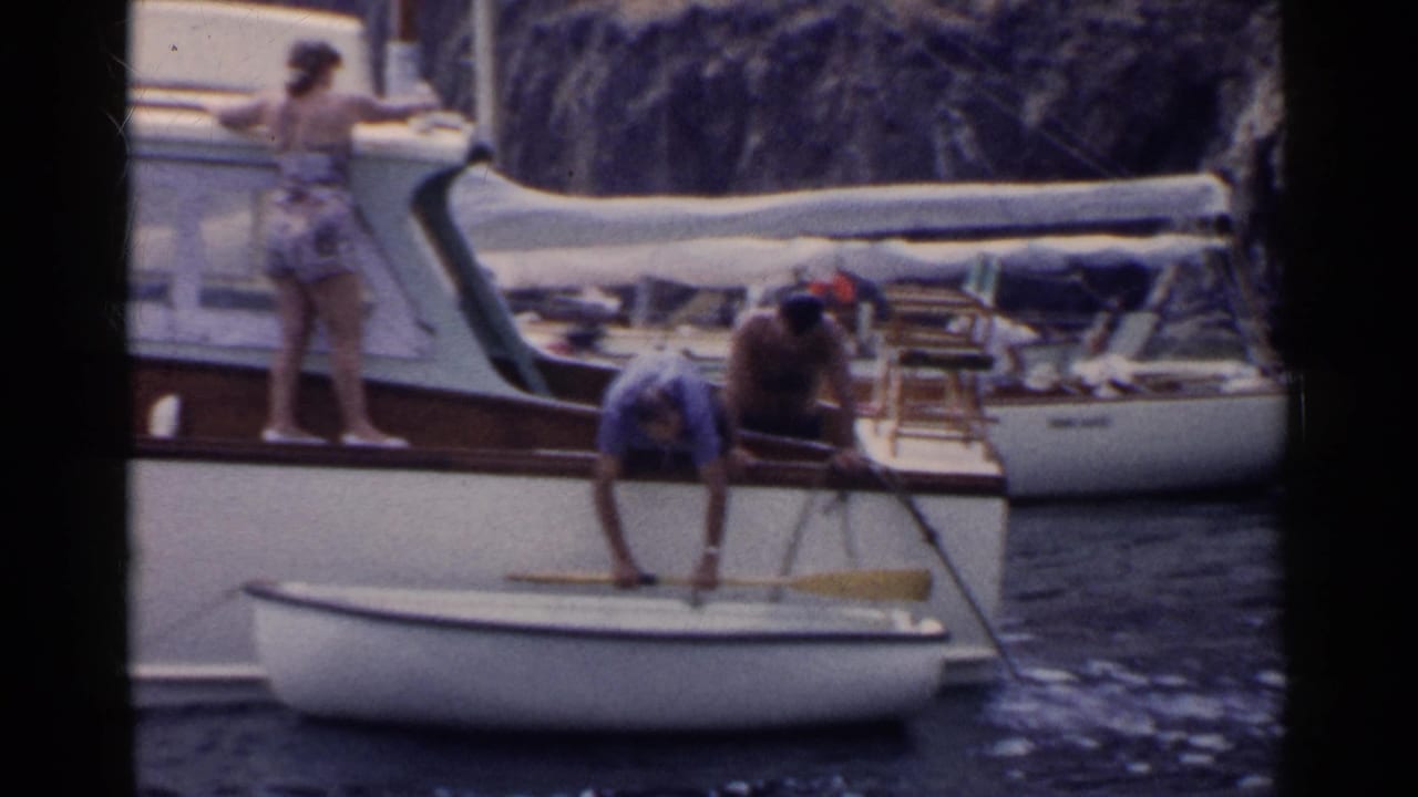 Adults stand and lean near a dinghy tied beside a white motorboat.