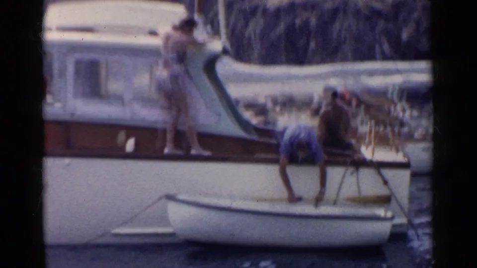 Soft 8mm frame from a 1955 California boat outing, with adults around a small dinghy tied beside a white motorboat.