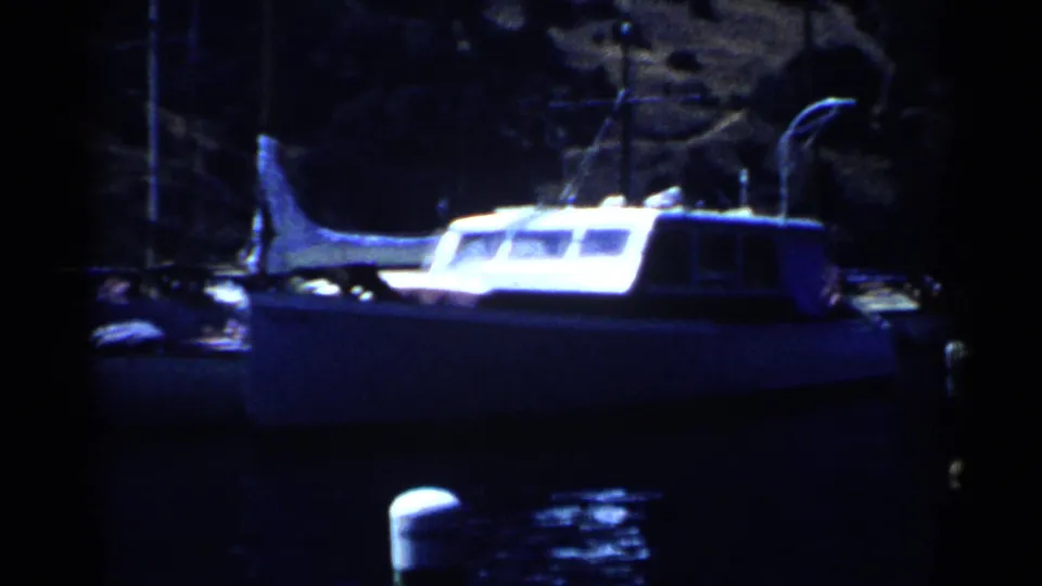 1955 California marina view with a white cabin motorboat on dark water against a rocky shoreline.