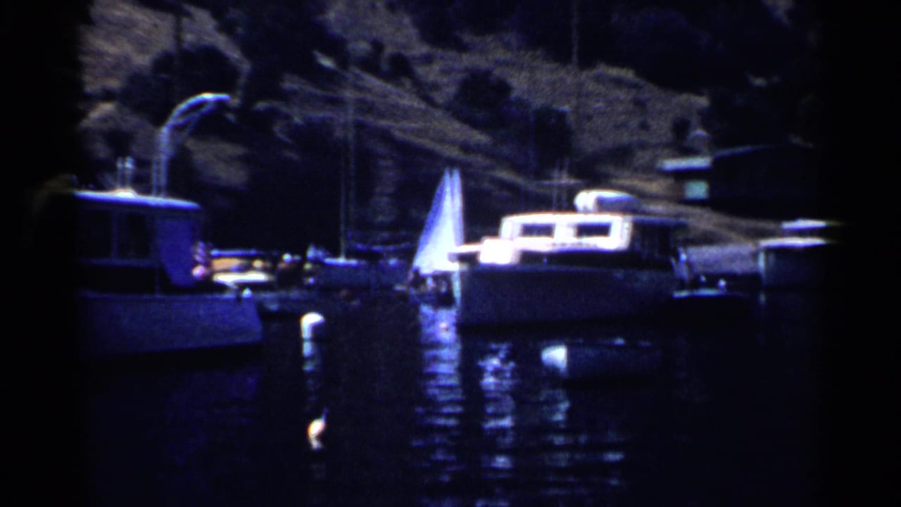 1955 California 8mm frame showing motorboats and a sailboat docked near a shadowed shoreline.