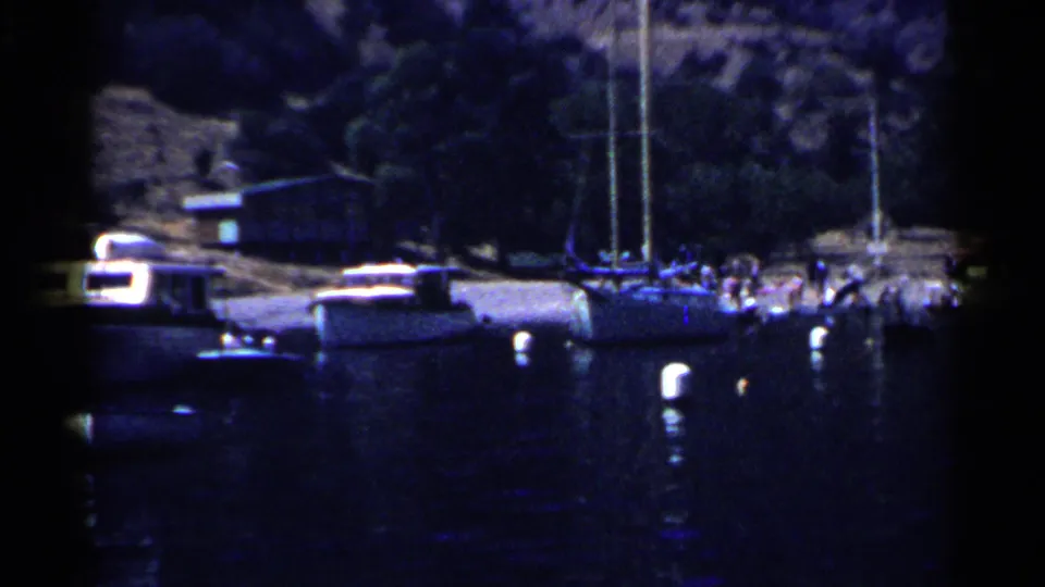 1955 California 8mm frame showing boats at a pier with distant people gathered along the waterfront.