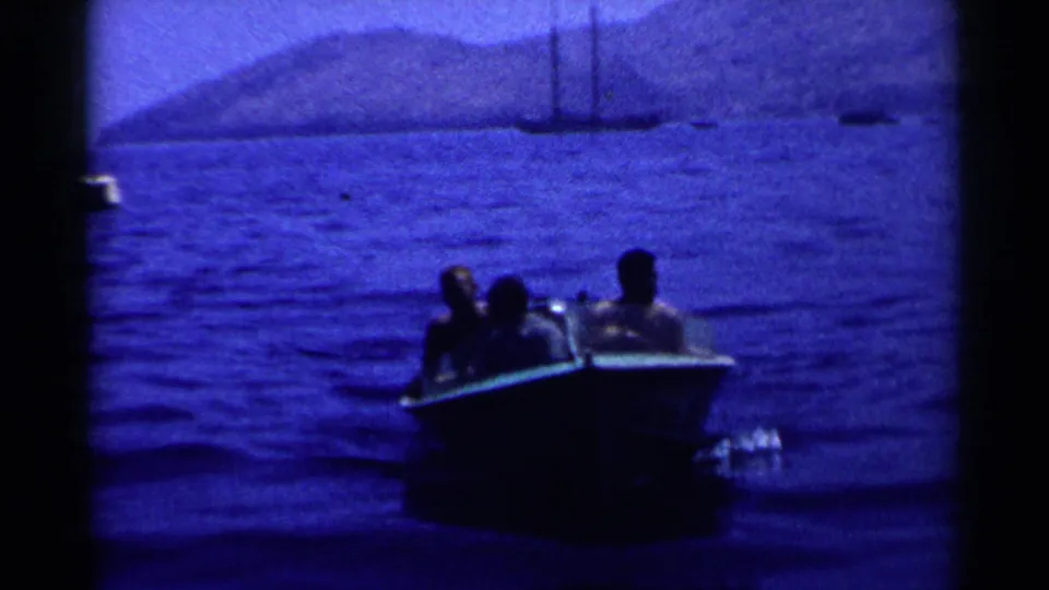 A small motorboat carrying three men moves through blue California coastal water in a 1955 home-movie frame.