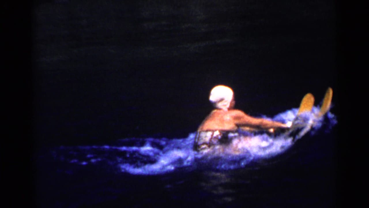 Woman in a white swim cap water skiing across dark blue water.