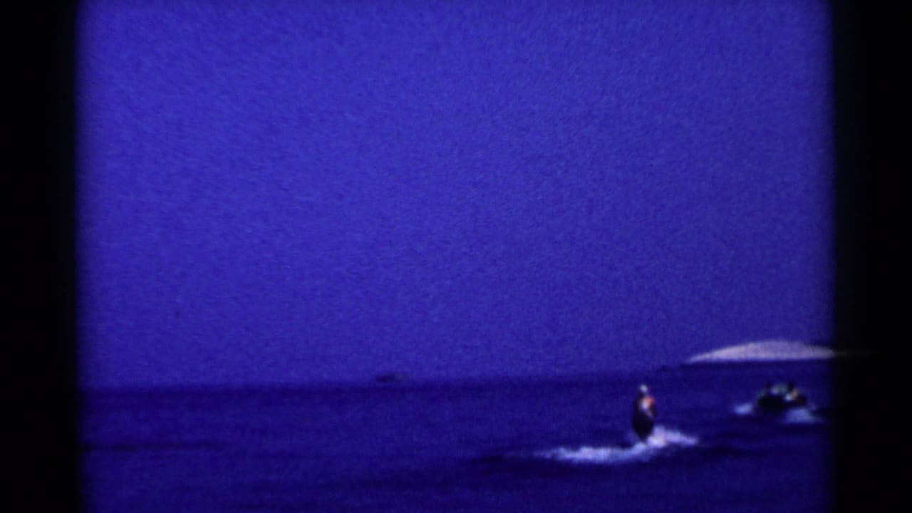 A distant view shows the skier and small tow boat on open blue water, with a low horizon in 1955 California home-movie footage.