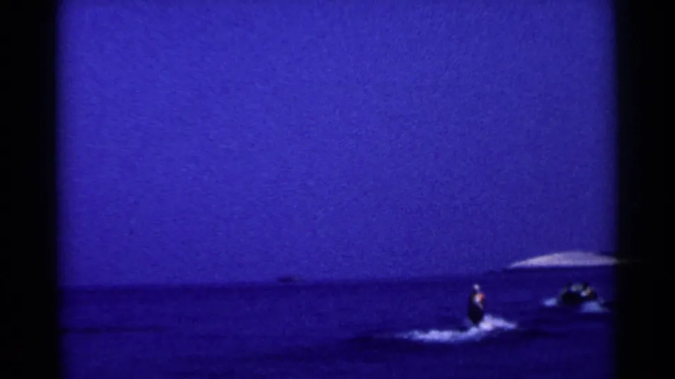A distant view shows the skier and small tow boat on open blue water, with a low horizon in 1955 California home-movie footage.