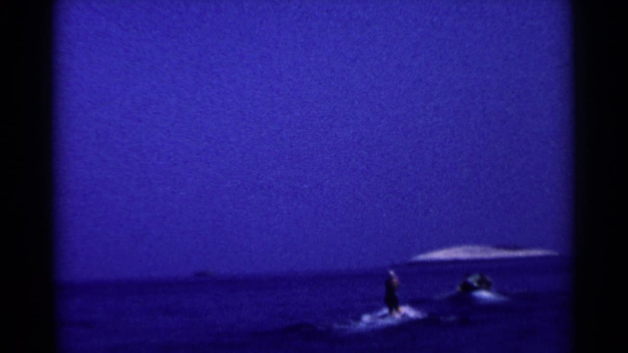 Distant water skier and motorboat on a dark lake under a blue sky.