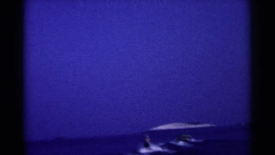 A distant skier trails near a small motorboat on a California lake in grainy 1955 home-movie footage.