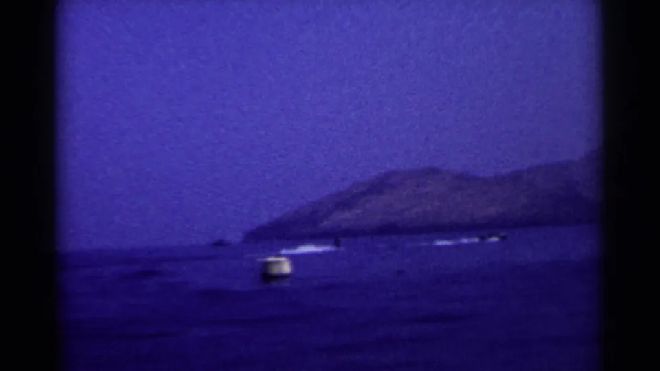 1955 California 8mm frame with a lake buoy, distant motorboats, low hills, and deep blue twilight exposure.