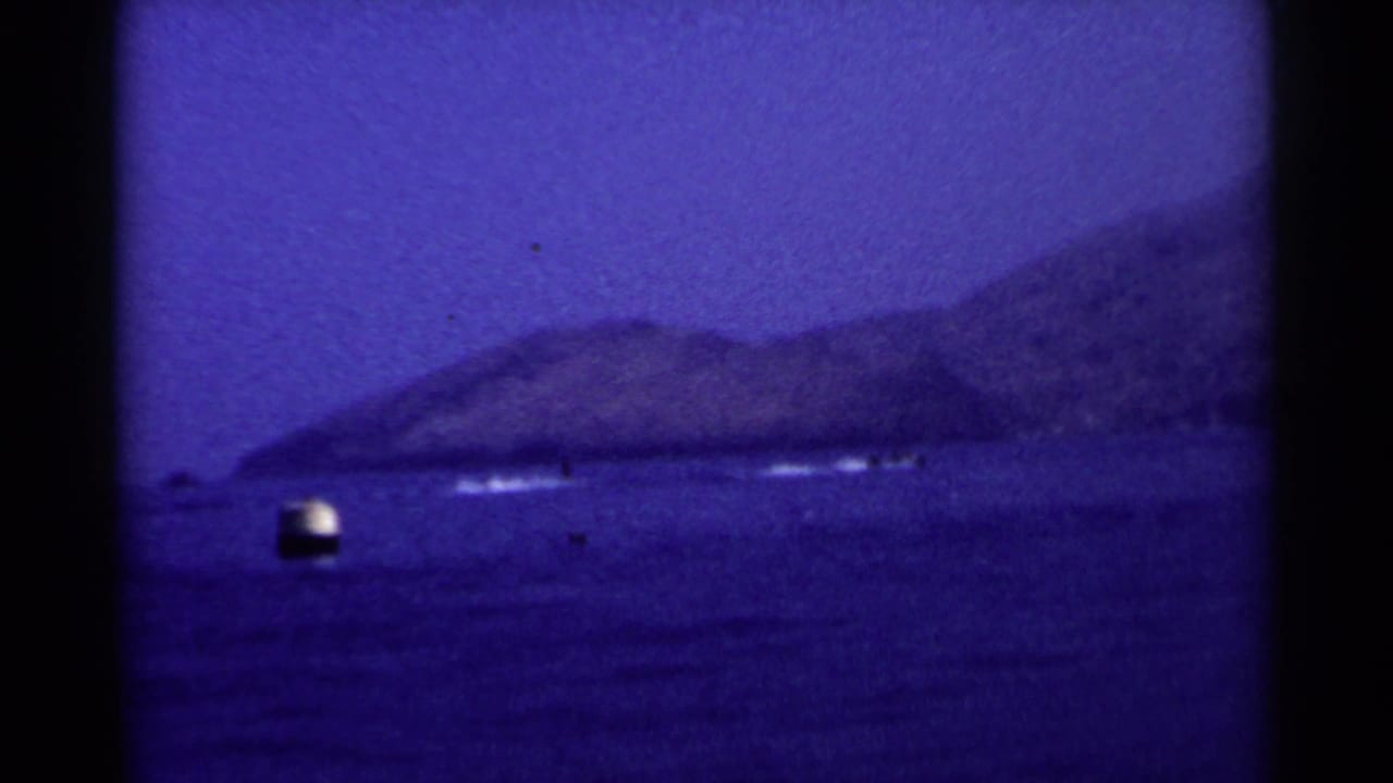 1955 California 8mm frame showing open blue water, a distant headland, and a small light buoy or boat near the left side.