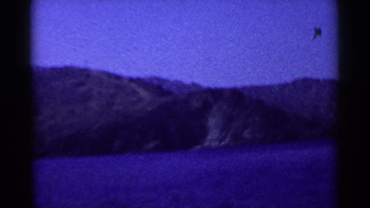 Rugged coastal hills across blue water, divided by dark film-frame borders.