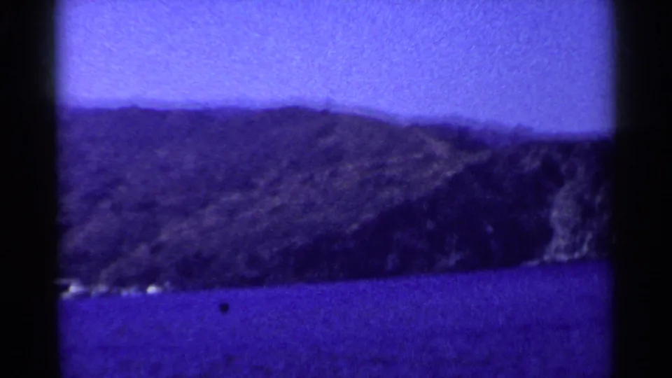 Blue-tinted 8mm coastal view in California, with rugged hills over water and visible gate edges and dust marks.