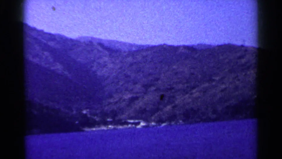 8mm home-movie frame from 1955 showing Lake Tahoe water and a sloping wooded hillside with small bright shoreline details.