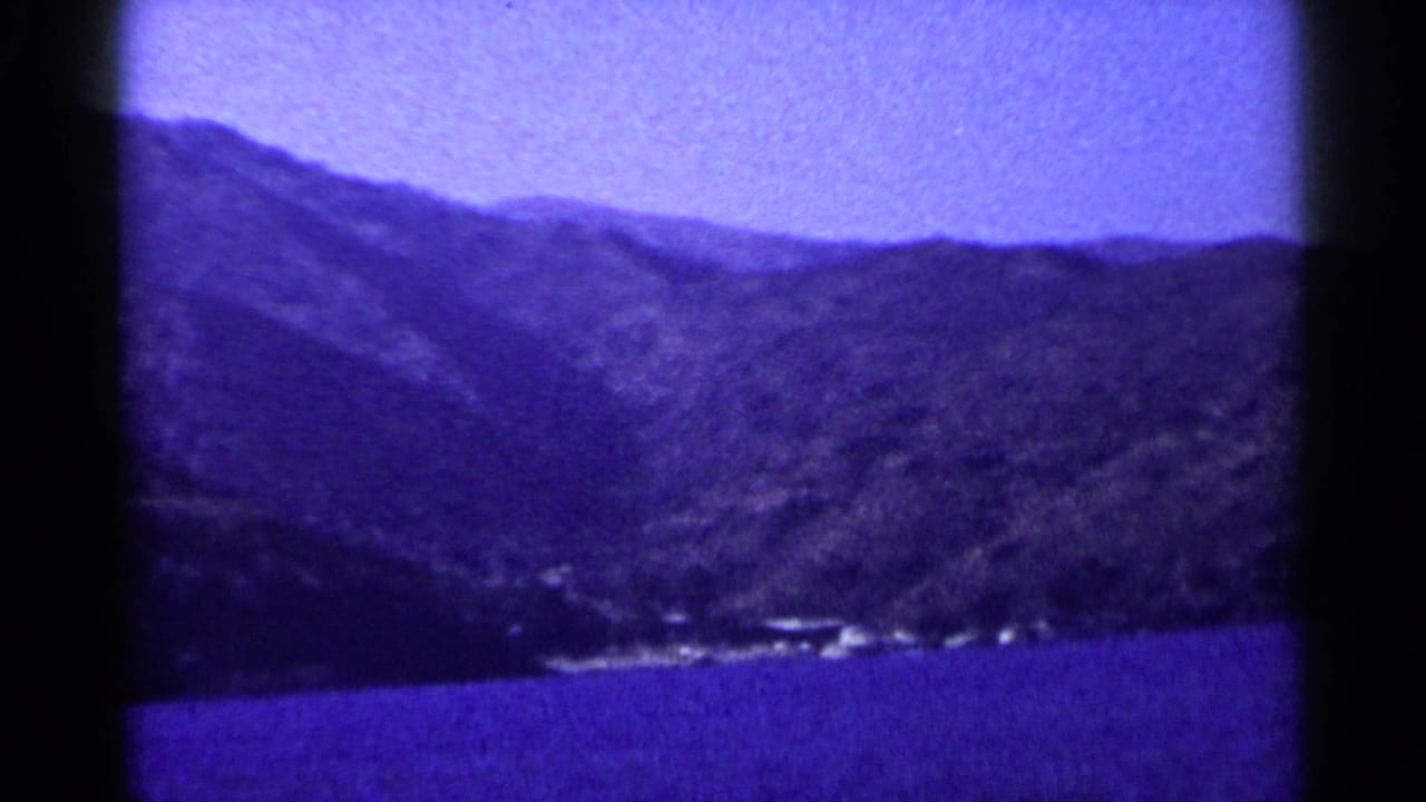 Mountain range above blue water with dark film borders.
