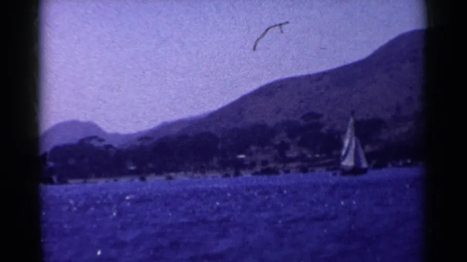 Final 1955 California frame showing the sailboat near the right edge against blue water, shoreline, and mountain terrain.