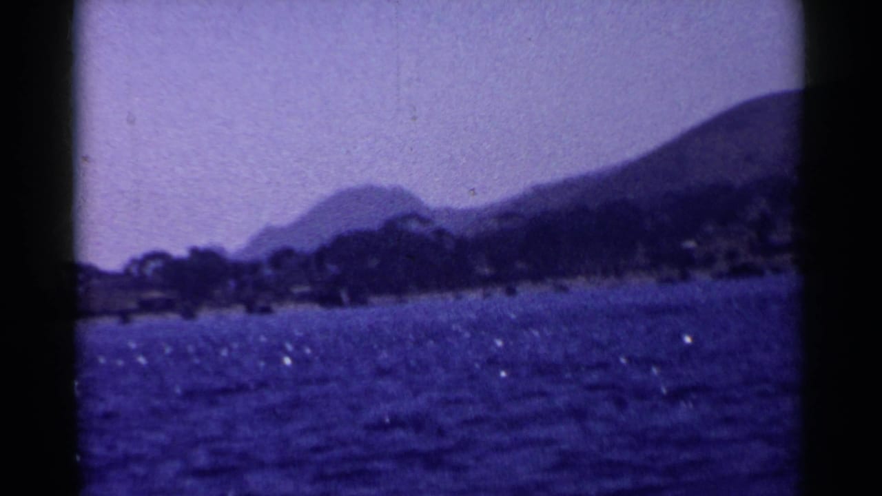 1955 California 8mm frame showing a blue lake, tree-lined shore, and hazy mountains with dark film-frame edges.