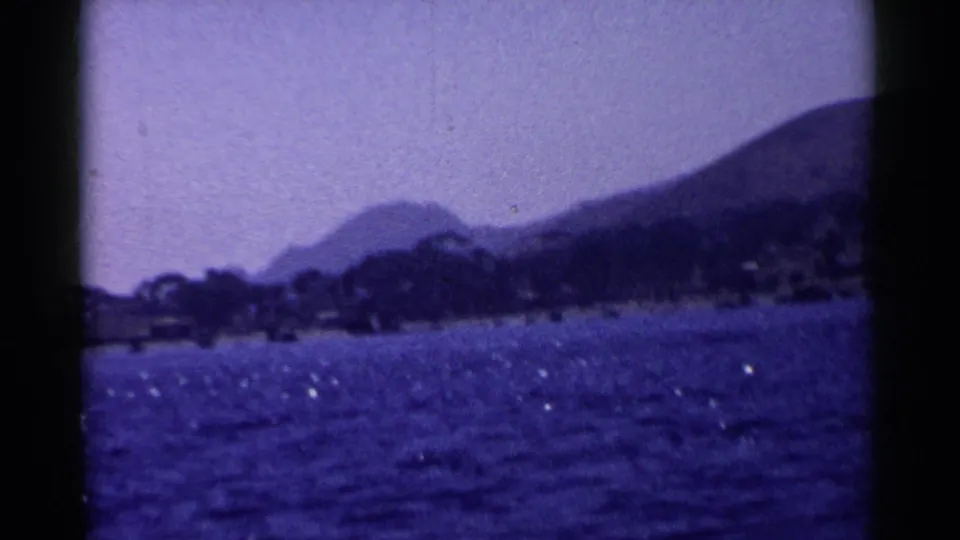 1955 California 8mm frame showing a blue lake, tree-lined shore, and hazy mountains with dark film-frame edges.