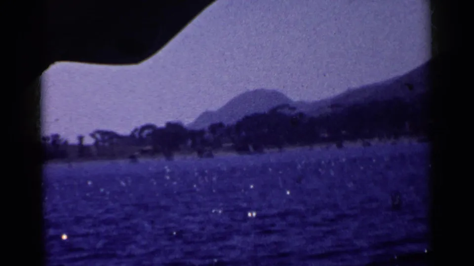 1955 California 8mm frame showing a blue lake and distant mountains, partly bordered by a dark film-gate shadow.