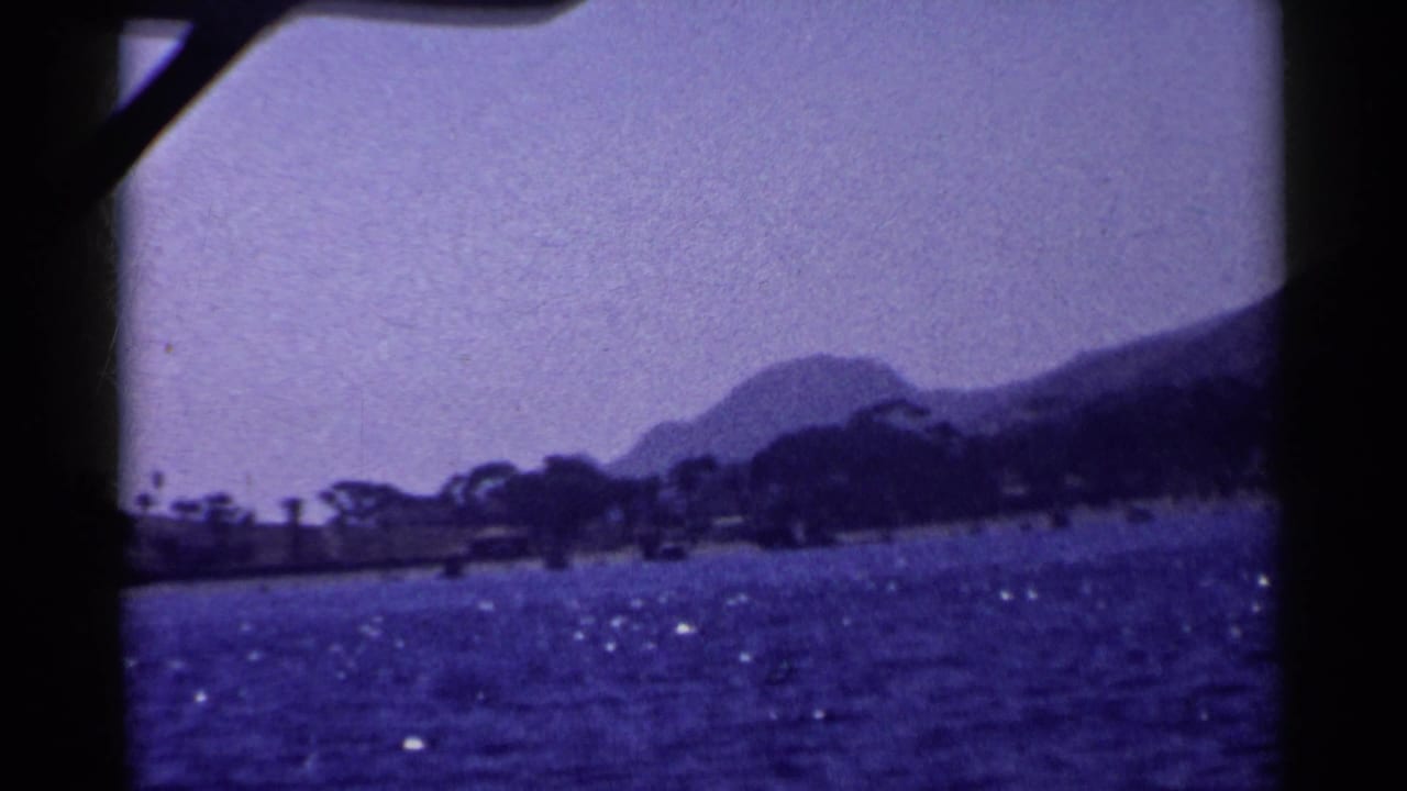 1955 California 8mm frame showing wavy water, sun glints, distant shoreline trees, and a mountain seen from a boat.