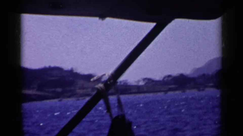 Final 1955 California frame shows dark boat rigging over choppy water, distant shoreline trees, and hazy mountain forms.