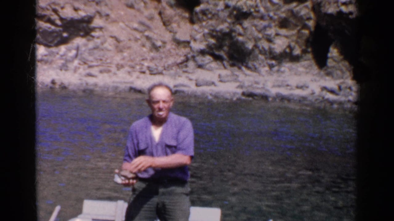 In 1955 California home-movie footage, a man in a purple shirt sits in a small boat near a rocky cliff while holding clams.