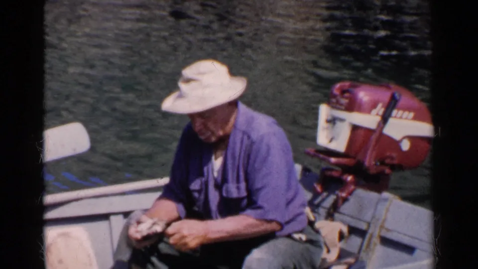 The man remains seated in the small motorboat, looking down as he handles clams with the red outboard motor visible at the stern.