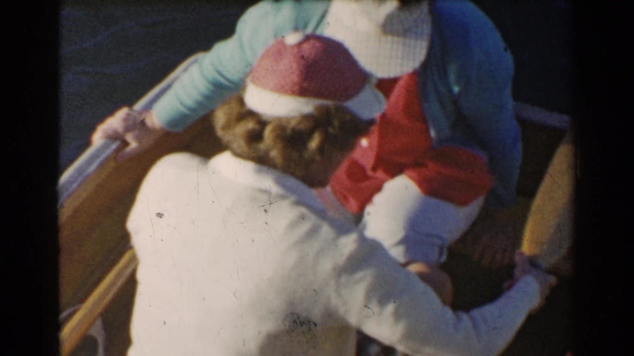 Two women in a wooden rowboat handle an oar on dark water.