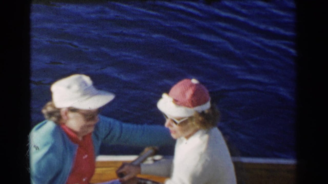 Two older women sit facing each other in a small wooden boat on blue water.