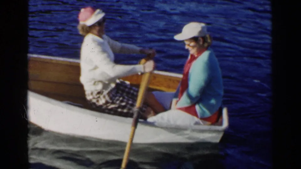 The final frame shows the women in profile in a small wooden rowboat, surrounded by blue lake water in 1955 California footage.