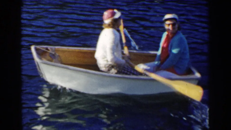 1955 California lake scene showing two women in a small rowboat, one turned toward the camera as an oar crosses the foreground.