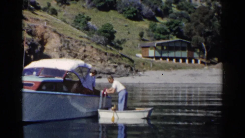 The final frame shows the man handling gear near the small dinghy and cabin cruiser, with calm water and hillside shoreline behind him.
