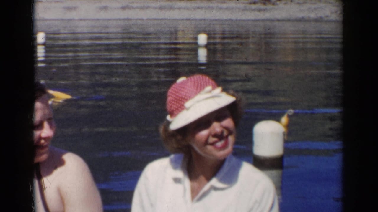 Two women by a pond, one partly cropped and one smiling in a sun visor.