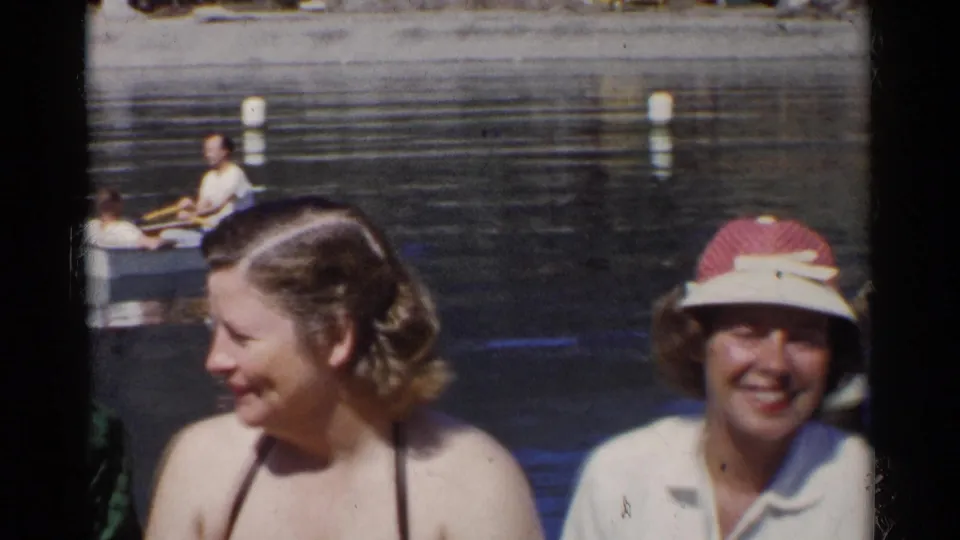 1955 California home-movie frame with women near the pond and a person rowing a small boat behind them.