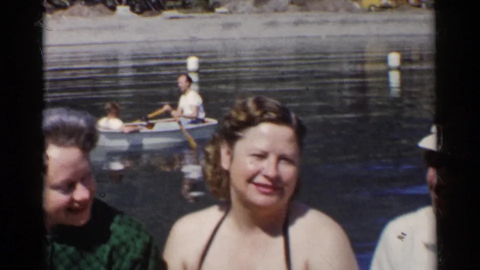 1955 California frame of women relaxing near a pond, with a small rowboat and white buoys in the background.