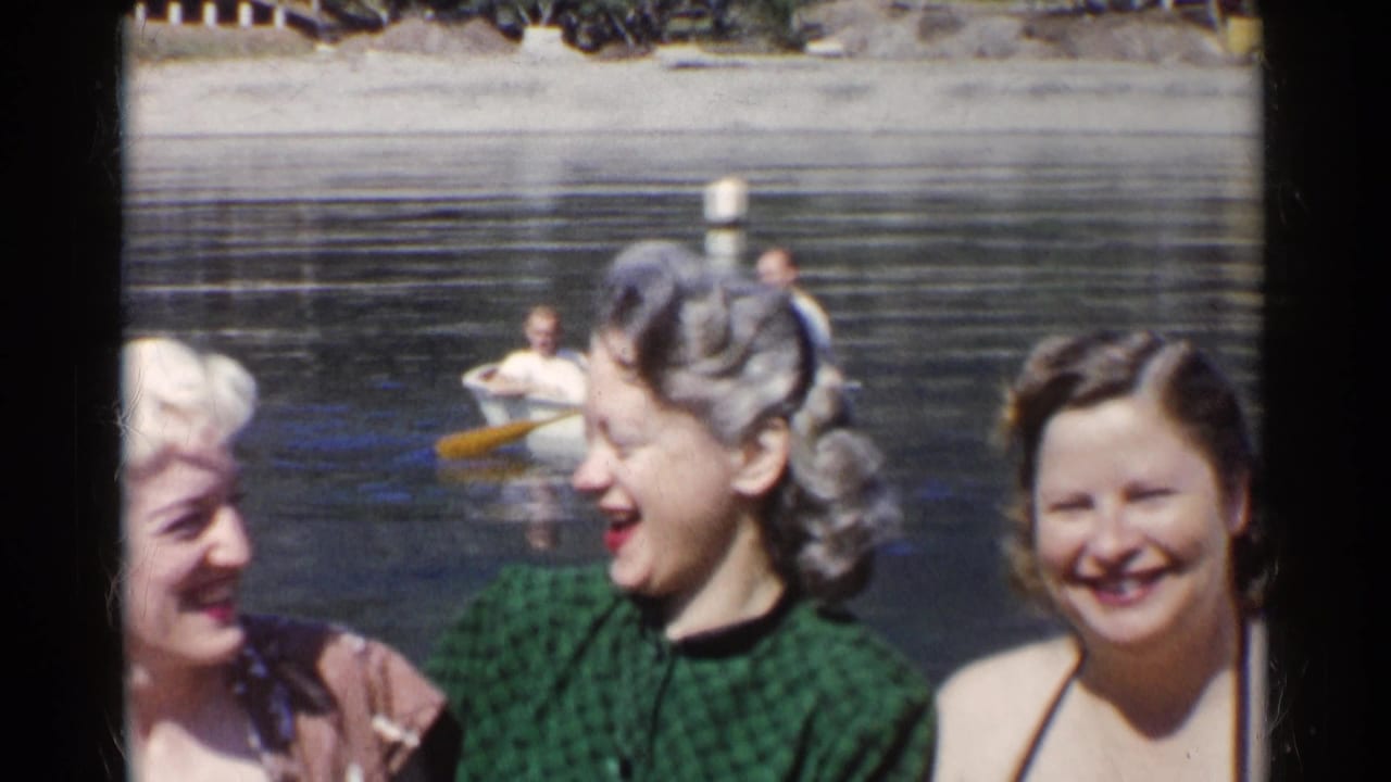 Three women on a lakeshore with a small rowboat visible behind them.
