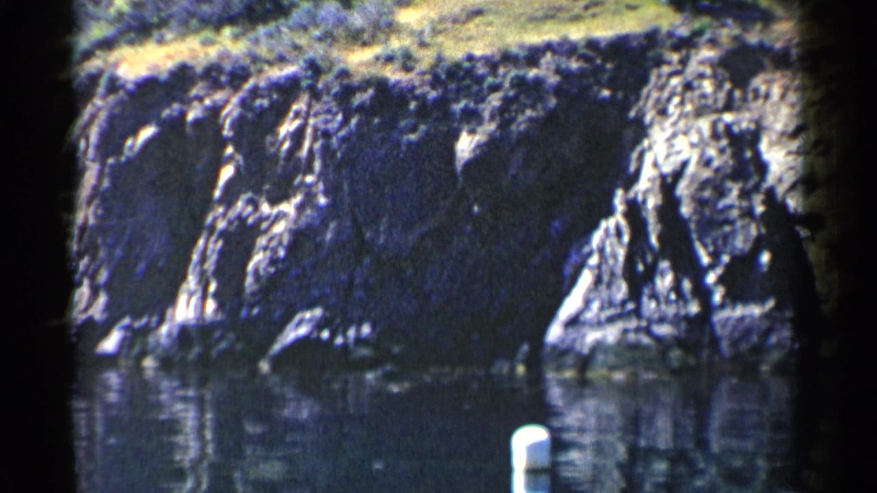 Rocky shoreline cliffs above calm water with a white buoy near the lower foreground.