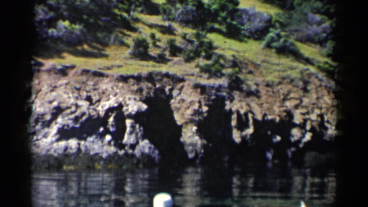 Rock ledge beside still water with hillside vegetation and film gate edges.