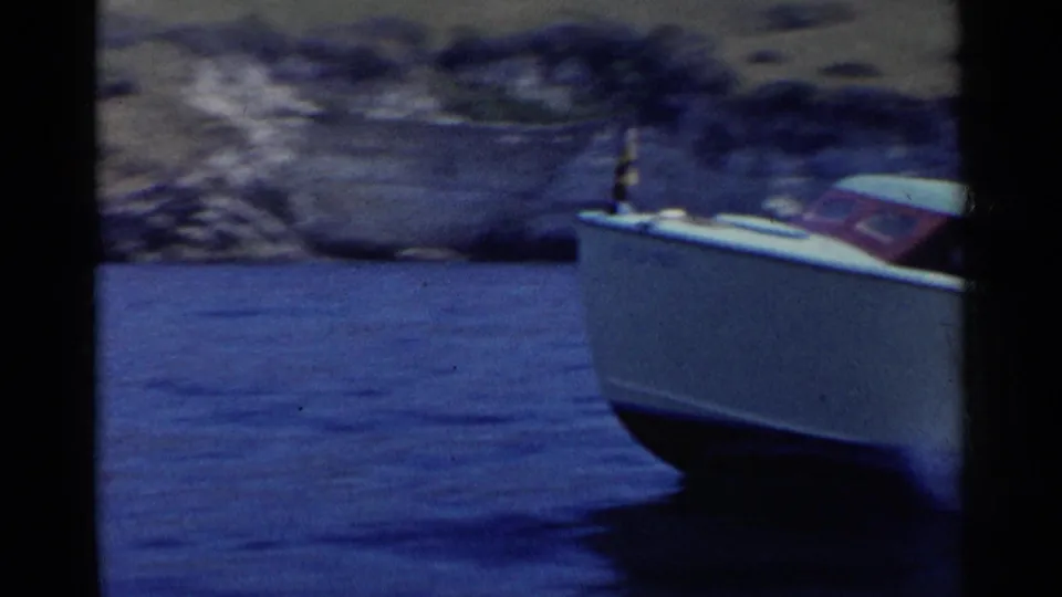 The motorboat passes partly out of frame on a California lake, with rocky shore and blurred hills in the background.