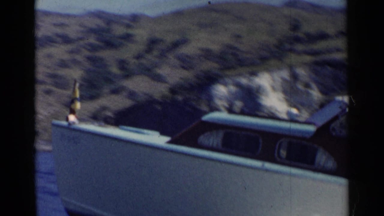 White speedboat with small flag passing rocky hills beside water.