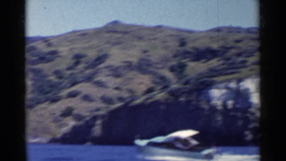 The speedboat appears farther away on blue water, framed beneath dry California hills and a pale sky.