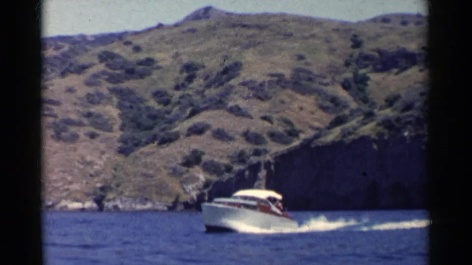 The boat appears farther along the shoreline, throwing a white wake against blue water below rugged California hills.