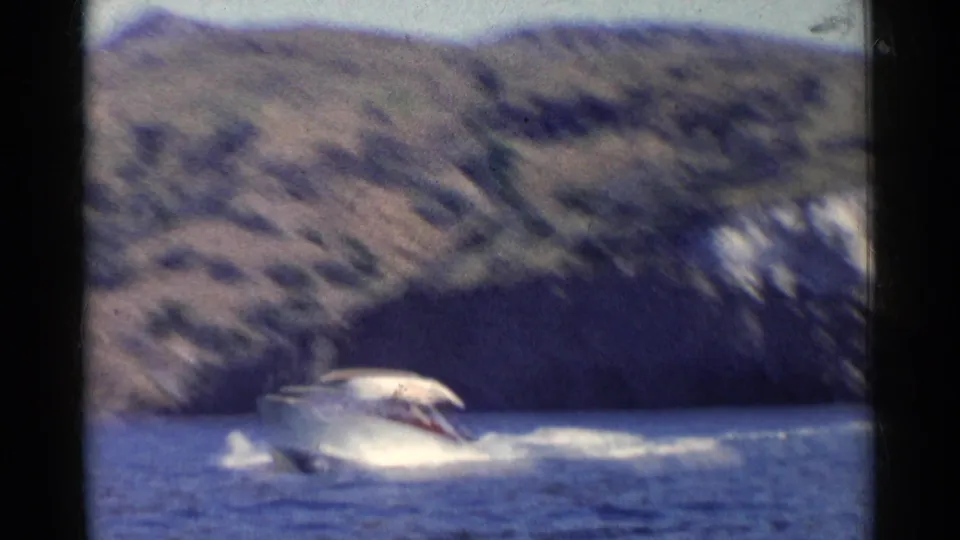 1955 California coastal home-movie frame with a white runabout moving across choppy blue water against arid hills.