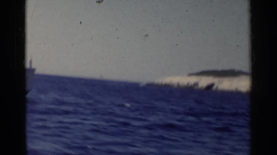 1955 California 8mm frame showing choppy blue water and a distant pale shoreline beneath a muted sky.
