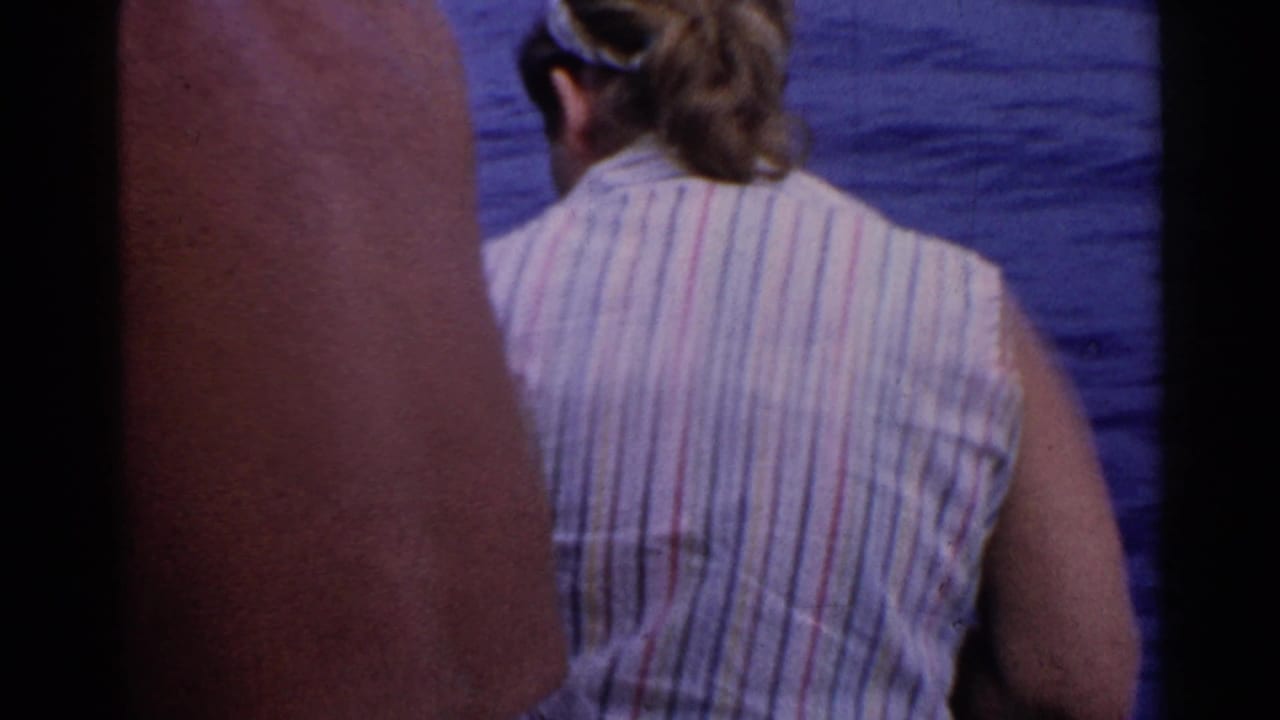 1955 California boat-ride frame showing the back of an adult in a striped sleeveless top near blue ocean water.