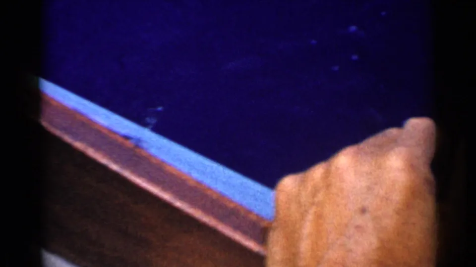 An adult hand rests near a boat edge while dark blue water fills the background in this 1955 California home-movie frame.