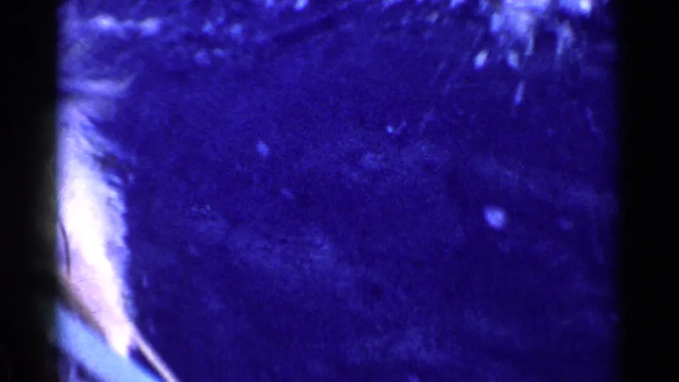 Grainy 8mm underwater view with deep blue color shift, dark frame edges, and indistinct shapes near the left side.