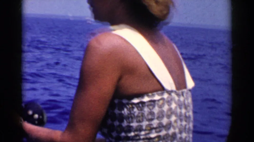 The woman remains turned toward the open ocean, holding fishing gear in a handheld 8mm view from a boat off California.
